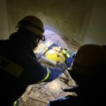 Ein Verletztendarsteller wird auf der metallenen Schleifkorbtrage von seinen Kameraden durch das schmale Loch in der Wand gezogen. (Foto: THW/Sandro Wiggerich)